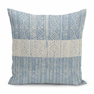 May include: A square throw pillow featuring a dusty blue and off-white color scheme. The design consists of horizontal bands displaying geometric patterns, including diamonds, triangles, and vertical chevron-like lines with a distressed texture.