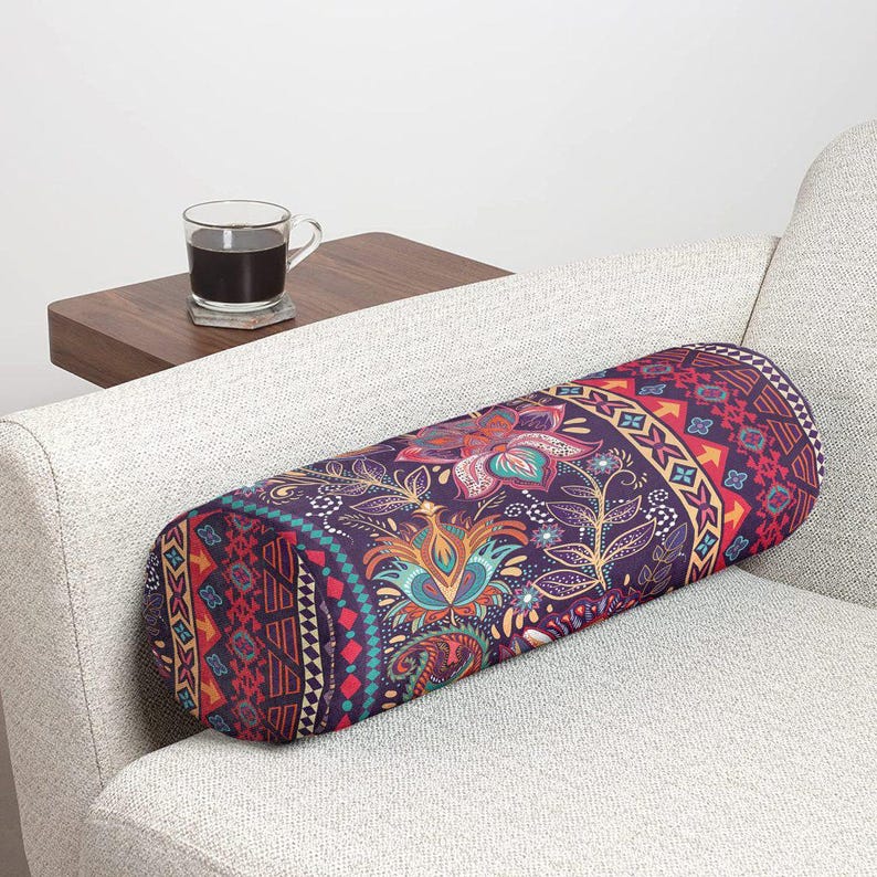 May include: A cylindrical bolster pillow featuring a dark purple base with a vibrant, multi-colored floral and geometric pattern. The design includes intricate paisley-like motifs, orange arrows, and teal accents, creating a detailed surface.