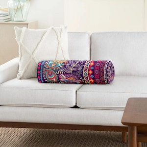 May include: A cylindrical bolster pillow featuring a vibrant purple base with a multi-colored paisley and geometric pattern, positioned alongside a square white throw pillow with a textured, crisscross tufted design on a white sofa.