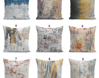 Può includere: Una collezione di nove cuscini quadrati con diversi motivi astratti. I design includono sfumature blu e bianche, toni della terra testurizzati, striature dorate e antracite, effetti marmo grigio e schizzi di vernice multicolore.