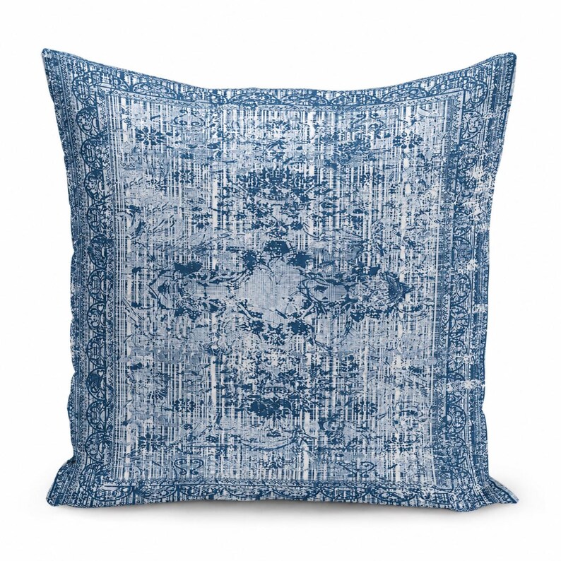 May include: A square throw pillow featuring a distressed, faded blue and white pattern. The design includes a central medallion motif surrounded by intricate floral and geometric borders, mimicking the appearance of a worn area rug.