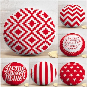 Könnte beinhalten: Eine Sammlung von sechs runden Zierkissen mit roten und weißen Mustern. Die Designs umfassen einen roten geometrischen Rautenaufdruck, ein rotes Zickzackmuster, ein weißes Kissen mit rotem Text home sweet home, ein rotes Kissen mit weißem Text home sweet home, rote vertikale Streifen und ein rotes Kissen mit weißen Sternen.