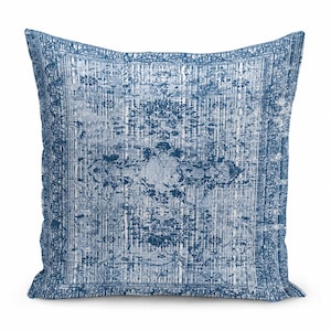May include: A square throw pillow featuring a distressed, faded blue and white pattern. The design includes a central medallion motif surrounded by intricate floral and geometric borders, mimicking the appearance of a worn area rug.