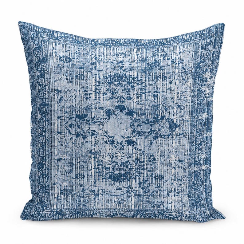 May include: A square throw pillow featuring a distressed, faded blue and white pattern. The design includes a central medallion motif surrounded by intricate floral and geometric borders, mimicking the appearance of a worn area rug.