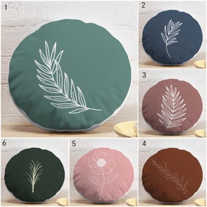 May include: Round decorative pillows in various colors, each featuring a white botanical design. Colors include teal, navy, mauve, brown, pink, and dark green. The pillows have a white border.