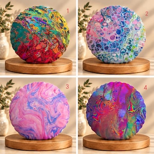 May include: Four round pillows with scalloped edges, each featuring a unique fluid acrylic pour pattern. Pillow 1 has warm tones, 2 has cool blues and pinks, 3 has soft pink and purple swirls, and 4 has a vibrant, iridescent holographic effect.