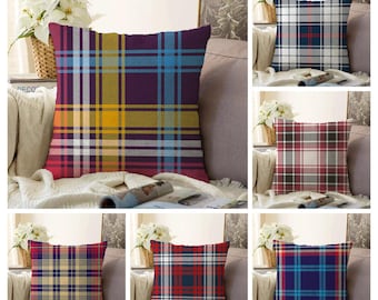 Op de afbeelding: Een collectie van zes vierkante sierkussens met diverse ruit- en tartanpatronen in kleurcombinaties van paars, geel, blauw, rood, wit en grijs. Elk kussen wordt getoond op een bank met een wit bloemstuk in de nabijheid.