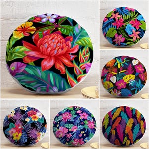 Puede incluir: Una colección de cojines redondos decorativos con vibrantes estampados florales y de hojas tropicales. Los cojines presentan una variedad de diseños coloridos, incluyendo grandes flores rojas, hibiscos rosas y plumas coloridas, sobre un fondo negro.