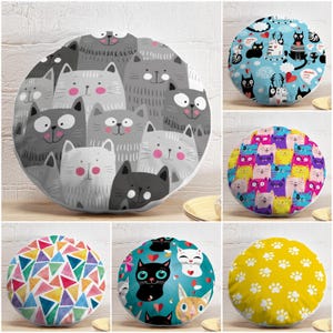 May include: A collection of six round scatter cushions featuring various patterns including grey and white cats, blue cats with hearts, colourful cats, geometric triangles, cats with red hearts on teal, and white paw prints on a yellow background.
