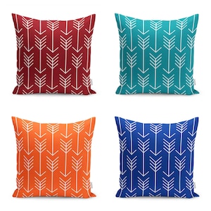 Op de afbeelding: Vier decoratieve kussens met een wit pijlpatroon op een effen achtergrond. De kussens zijn in de kleuren rood, turquoise, oranje en blauw.