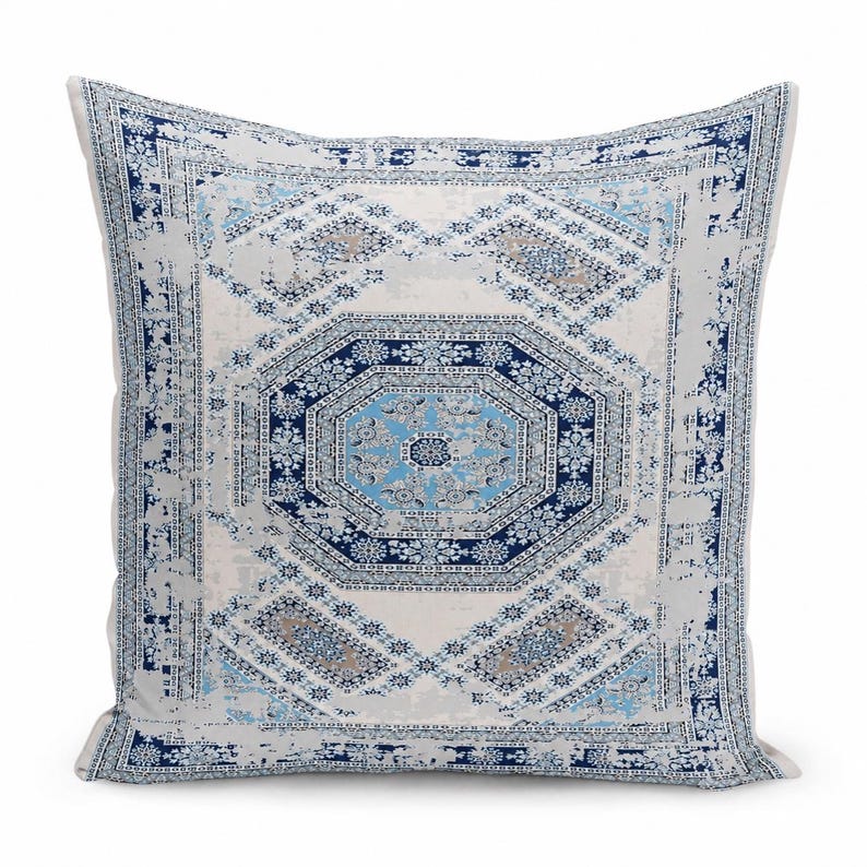 May include: A square throw pillow featuring a central octagonal medallion pattern in shades of navy blue, light blue, and white. The design includes intricate geometric and floral motifs with a distressed, weathered texture throughout the fabric.