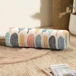 May include: A cylindrical cushion with a white background and a colourful pattern of stylised leaves. The leaves are in shades of blue, green, orange, and yellow.