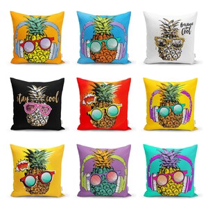 Pode incluir: Um conjunto de nove almofadas quadradas com várias ilustrações coloridas de abacaxis. Cada abacaxi usa auscultadores e óculos de sol, com alguns designs incluindo textos como 'Because I'm cool', 'stay cool' ou 'POW' num estilo pop art vibrante.