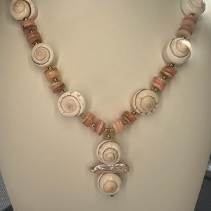 May include: A white seashell necklace with pink and gold beads. The necklace has a pendant with three white seashells.