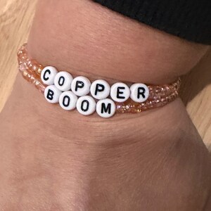 May include: A beaded bracelet with the words "COPPER BOOM" spelled out in white beads with black lettering.