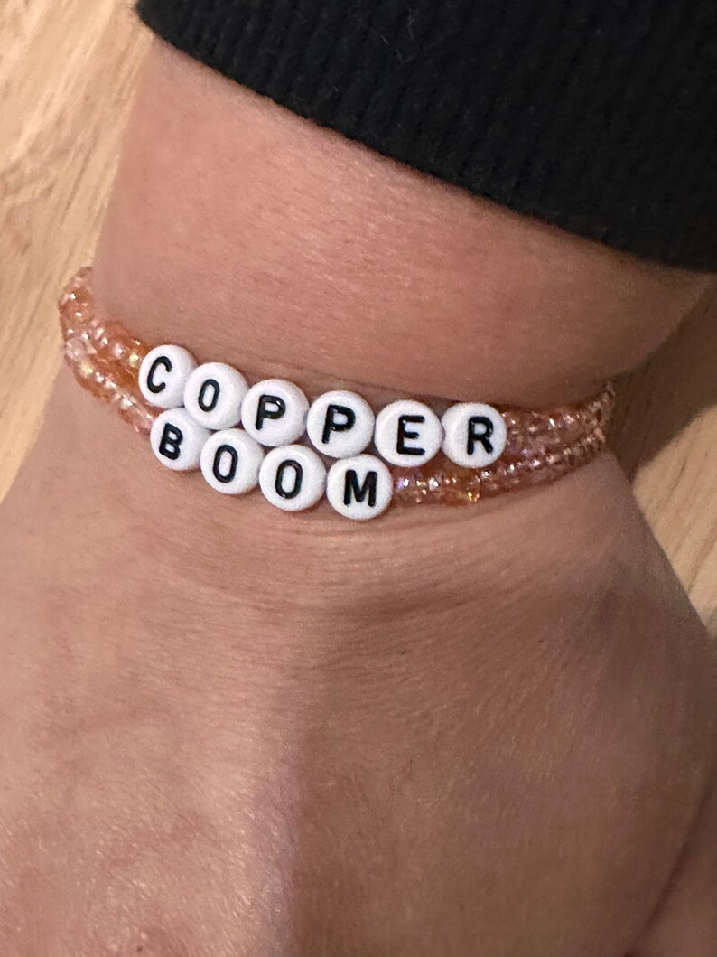 May include: A beaded bracelet with the words "COPPER BOOM" spelled out in white beads with black lettering.