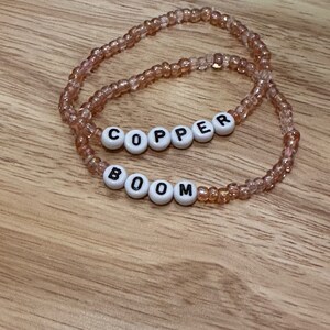 May include: Two beaded bracelets with the words "BOOM" and "COPPER" spelled out in white beads with black lettering.