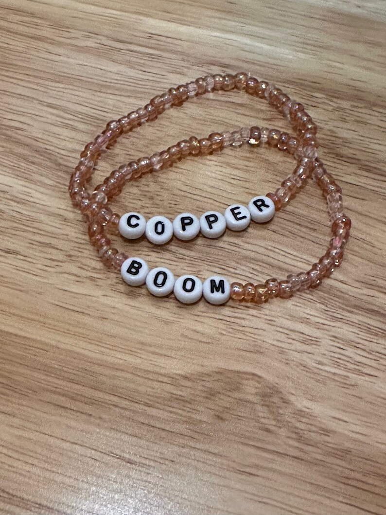 May include: Two beaded bracelets with the words "BOOM" and "COPPER" spelled out in white beads with black lettering.