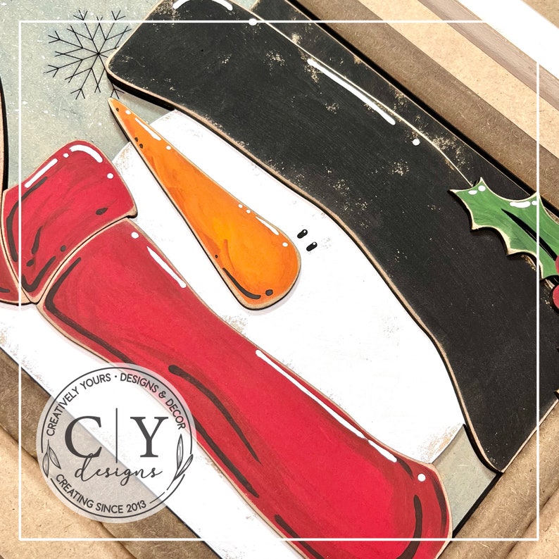 May include: A wooden snowman craft kit with a red hat, black top hat, white body, orange nose, and black eyes. The kit includes a holly sprig with red berries. The kit is made by "CY Designs" and says "Creating Since 2013".