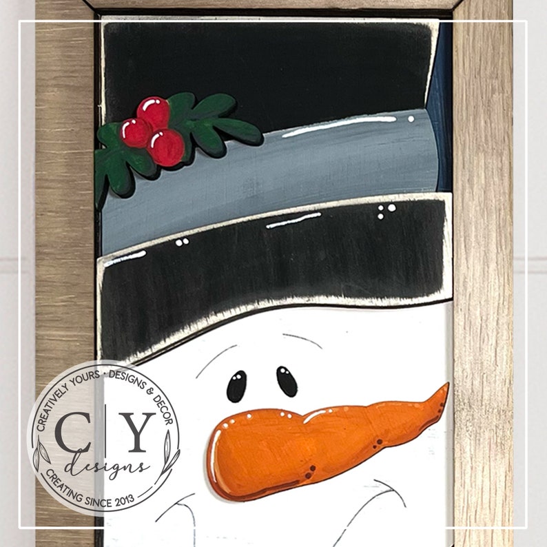 May include: A painted wooden snowman with a black hat, a gray brim, and a red holly sprig. The snowman has a carrot nose, black eyes, and a white face.