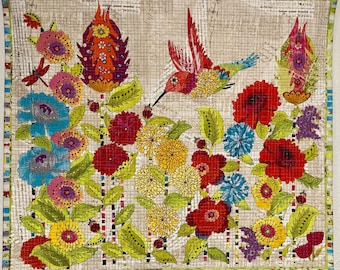 May include: A colorful patchwork quilt featuring a hummingbird in flight, surrounded by flowers in shades of red, yellow, blue, and green. The quilt is made of fabric squares sewn together to create a unique and intricate design.