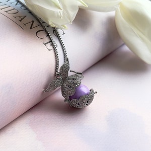 Puede incluir: Un collar de cadena de plata con un colgante con un diseño de mariposa detallado. La mariposa encierra una esfera de vidrio púrpura.