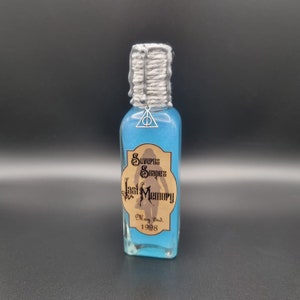 May include: A glass bottle filled with blue liquid, labeled "Severus Snape's Last Memory, May 2nd, 1998." The bottle has a silver-colored top with a rope-like texture and a silver charm with a triangle and a line through it.