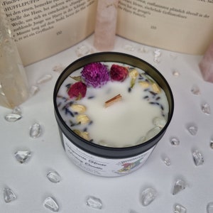 Könnte beinhalten: Eine schwarze Metallkerze mit weißem Wachs, getrockneten Blumen und Kristallen. Die Kerze hat einen Holzdocht und ist mit rosa und lila Blüten verziert. Das Etikett lautet "Hogwarts House Healing Candle."