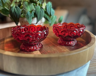 Puede incluir: Dos cuencos pequeños de vidrio rojo vibrante con un patrón en relieve de lunas y estrellas en el exterior. Cada cuenco tiene un borde festoneado y una base circular con pedestal, hechos de vidrio rojo translúcido con acabado brillante.