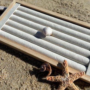 May include: A white seashell ring on a beige ring display stand with a starfish and a seashell on a sandy background.