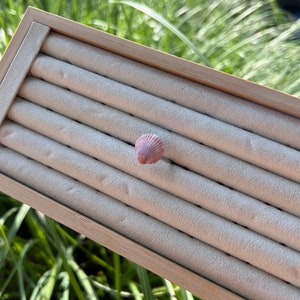 Peut inclure: Une boîte à bagues en bois avec un intérieur en velours blanc. La boîte comporte huit fentes pour les bagues. Un petit coquillage rose se trouve dans l'une des fentes.
