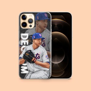 Op de afbeelding: Transparante telefoonhoes met een honkbalspeler in een Mets-uniform. Het ontwerp bevat een portret van de speler en de naam "DeGrom" in het wit. De hoes wordt getoond naast een leeg telefoon.