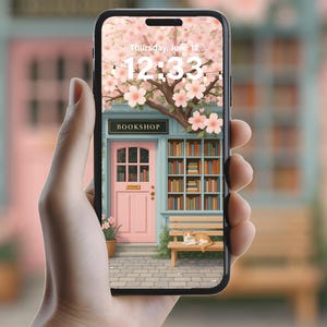 May include: A smartphone screen shows a picturesque bookshop scene with a pink door, a bench, and a cat, framed by a flowering tree. The image includes the text "BOOKSHOP" and the time 12:33. The phone is held in a hand.