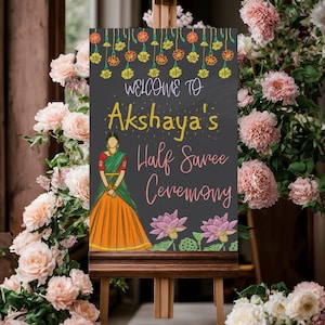 May include: A chalkboard sign with a floral border and the text "Welcome to Akshaya's Half Saree Ceremony". A cartoon illustration of a woman in a traditional Indian outfit is featured on the sign.