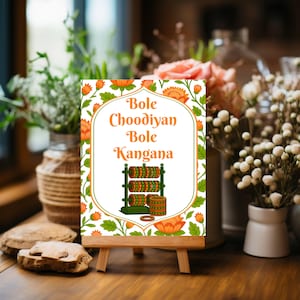 Könnte beinhalten: Ein dekoratives Schild auf einer Holzstaffelei zeigt den Text "Bole Choodiyan Bole Kangana" in orangefarbener Schrift. Das Schild ist mit orangefarbenen und grünen Blumen- und Blättermotiven verziert und zeigt bunte Armreifen.