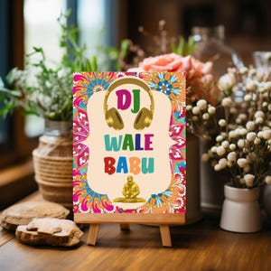 May include: A colourful sign on a wooden easel features the words "DJ WALE BABU" with a gold headphone graphic. The sign has a beige background with a vibrant floral design in shades of pink, blue, orange, and yellow.