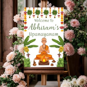 May include: Welcome to Abhiram's Upanayanam sign with a cartoon illustration of a person in a yellow robe meditating with a fire in front of them. The sign is decorated with green leaves, yellow flowers, and red flowers.