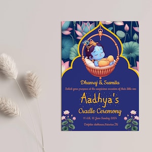 May include: A blue and gold invitation card with a floral design. The card announces a cradle ceremony for a baby boy named Aadhya. The text on the card reads "Dhanraj & Susmita Solicit your presence at the auspicious occasion of their little son Aadhya's Cradle Ceremony 4:1 AM, 18 June Sunday 2024 Dolphin clubhouse, Fuisine, TX."