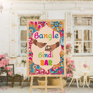 Puede incluir: Un letrero de madera con un dise&ntilde;o floral colorido y el texto "Bangle Bindi Bar". El letrero est&aacute; en un caballete y est&aacute; frente a una pared de ladrillo con una ventana.