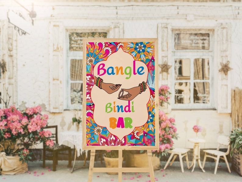 Puede incluir: Un letrero de madera con un dise&ntilde;o floral colorido y el texto "Bangle Bindi Bar". El letrero est&aacute; en un caballete y est&aacute; frente a una pared de ladrillo con una ventana.