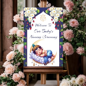 Könnte beinhalten: Ein Willkommenszeichen für eine Baby-Namensgebung mit blauem Hintergrund und weißen Blumen. Das Schild lautet "Willkommen zur Namensgebung unseres Babys". Eine Illustration eines schlafenden Baby Krishna auf einem Halbmond befindet sich unten in der Mitte des Schildes.