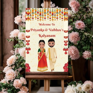 May include: A wedding welcome sign on a wooden easel. The sign features the text "Welcome To Priyanka & Vaibhav's Kalyanam" with illustrations of a couple in traditional Indian attire. Floral garlands and pink roses surround the sign.