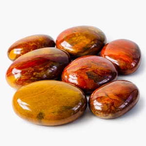 May include: A collection of polished stones in shades of red, orange, and yellow. The smooth, rounded stones have a glossy finish, with visible patterns and variations in color. The stones are arranged on a white surface.