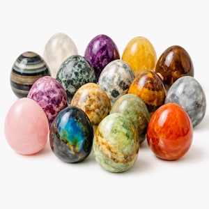 May include: A collection of fifteen polished gemstone eggs in various colors and patterns. The eggs include shades of pink, purple, green, yellow, brown, and gray. Each egg has a smooth, glossy surface, and they are arranged on a white background.