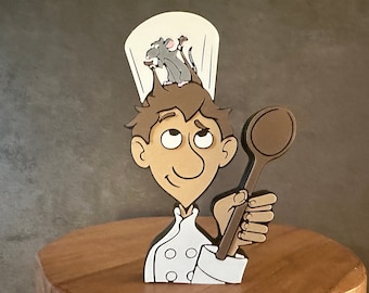 May include: A wooden figurine of a chef with a white chef's hat and a brown wooden spoon. Two small mice are on top of the chef's hat.