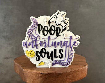 May include: White sign with purple and black lettering that reads "Poor unfortunate souls". The sign has a purple sea serpent design and a yellow seashell.