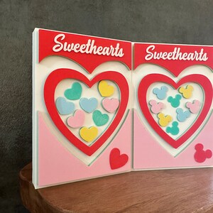 May include: Two white cardstock Valentine's Day cards with red hearts and the text "Sweethearts" on each card. The hearts are filled with colorful candy hearts and Mickey Mouse heads.