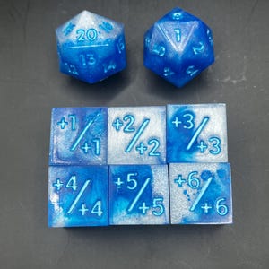 May include: A set of blue and white dice with silver glitter. The set includes a twenty-sided die, a six-sided die, and six smaller dice with numbers 1 through 6 and plus signs.