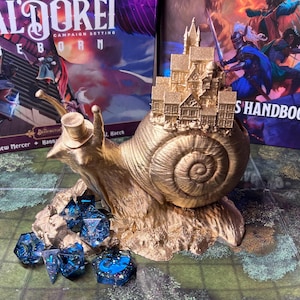 May include: A golden snail figurine with a miniature town on its back, wearing a top hat. Several blue and black dice are in front of the snail. The background includes two books with the titles "TAL'DOREI REBORN" and "PLAYER'S HANDBOOK".