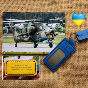 Peut inclure: Image d'un hélicoptère militaire, d'un cœur bleu et jaune et d'un porte-clés en cuir bleu. Le porte-clés porte l'inscription "Recyclé en Ukraine" et une petite étiquette indiquant "Fabriqué en Ukraine". Une étiquette jaune indique "Russian Mi-28N Battle for Hostomel Airport 25 February 2022, Ukraine."